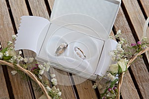 Two wedding rings in white case in wooden background with flowers