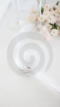Two wedding rings on white ribbon. Light blur background of flowers and champane glasses .