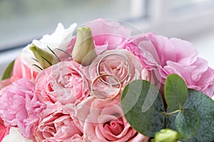 Two wedding rings of white and yellow gold on a bouquet of pink roses.