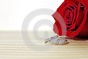 Two wedding rings on the wooden table with dark red rose.