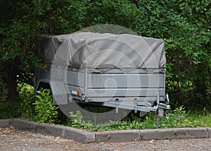 Two-wheeled gray awning trailer for a passenger car stands on a green lawn