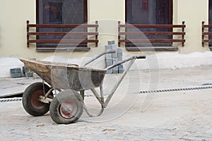 Two-wheeled wheelbarrow on a construction site of a granite pavement with grey regular and even stone blocks