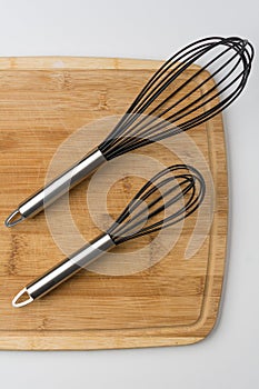 Two Whisks Angled on Wooden Cutting Board on White Background