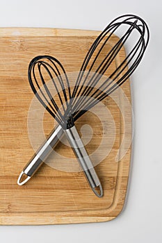 Two Whisks Crossed on Wooden Cutting Board