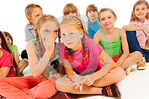 Two whispering girls sit among other friends