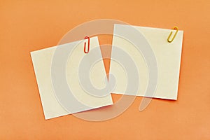 Two white adhesive note papers with clips on orange background