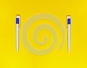 Two white ballpoint pens on a yellow background. Flat lay, copy space