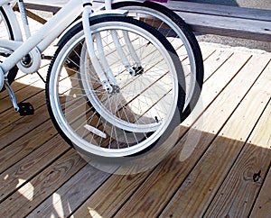 Two white bicycles resting dockside on a sunny day, cropped on front wheels