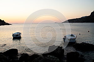 Two white boats in the sea water at sunrise. Calm seascape of sun rising over sea bay. Moored boats in the sea with sun