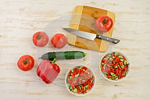 Two white bowls with fresh salad of green cucumbers, red tomatoes and bell peppers on light wooden surface. Vegetables. Lowcalorie
