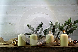 two white burning candles on the second advent, christmas decoration with spruce twigs, baubles and a golden ribbon on a rustic w