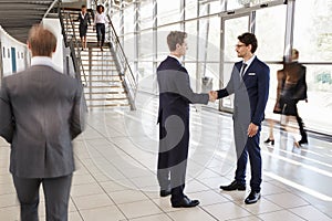 Two white businessmen shaking hands in a busy modern lobby