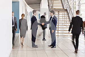 Two white businessmen shaking hands in a busy modern lobby