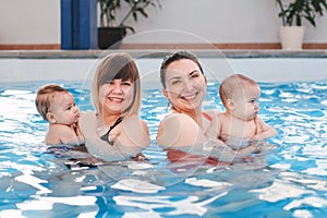 Two white Caucasian mothesr traning their newborn babies to float in swimming pool.