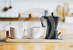 Two white ceramic mugs and geyser coffee maker on wooden tray on the kitchen table