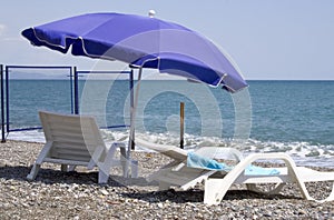 Two white chaise lounges stands on seacoast