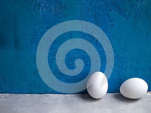 Two white chicken eggs on a blue and grey background.