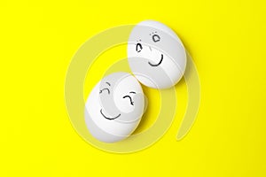 Two white chicken eggs with smiling faces on yellow background