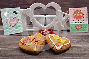 Two white cups of coffee, cookies in the shape of a heart, red candle and a Valentine card on a wooden table