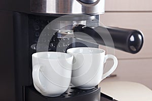 Two white cups for coffee under carob coffee maker