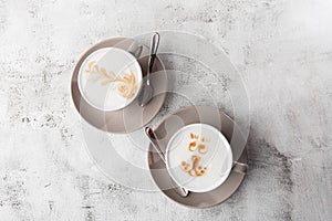 Two white cups of hot latte coffee with beautiful milk foam latte art texture isolated on bright marble background. Overhead view
