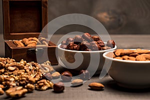 Two white cups with nuts, almonds, hazelnuts, walnut and a wooden box with almonds, side view