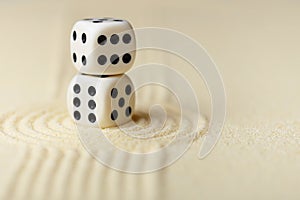 Two white dice with black dots on sand