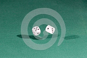 Two white dices falling on a green table