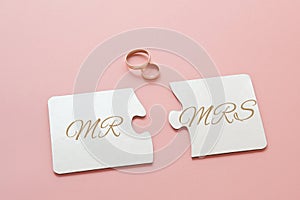 two white disconnected puzzles with the inscription Mr. and Mrs. and two gold wedding rings on a pink