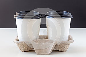 Two white disposable cups with lids in a cardboard tray