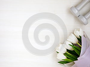 Two white dumbbells and tulips on white background with copyspace.