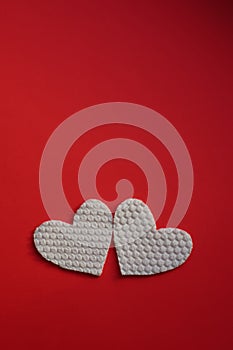 Two white fabric hearts on vivid red table. Art card