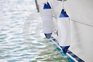 Two white fenders suspended between a boat and dockside for protection. Maritime fenders