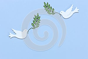 Two white figurines of a doves of peace with olive tree branch in their beaks on the light blue background. Peace Concept