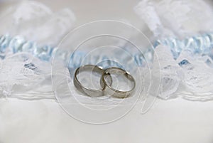 Two white gold wedding rings on white lace pad and blue garter