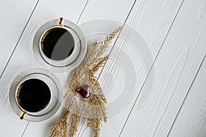 Two white and golden cups of coffee with decorative golden branches and small glass hearts on white wooden background