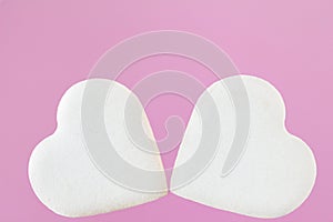 Two white heart shaped cookies on light pink background.