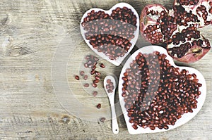 Two white heart shaped plates full of fresh juicy pomegranate seeds, little spoon, whole fruit and ripe one. Toned.