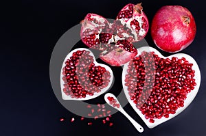 Two white heart shaped plates full of fresh juicy pomegranate seeds, little spoon, whole fruit and ripe one. Toned.