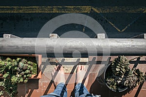 Two white man naked feet on the edge of a balcony with a metal fence