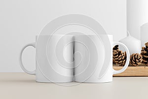 Two white mugs mockup with candles on a table. Christmas decoration