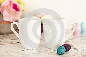 Two White Mugs Mockup - Easter theme. Easter eggs. Colorful eggs in matte colors. Light marble background