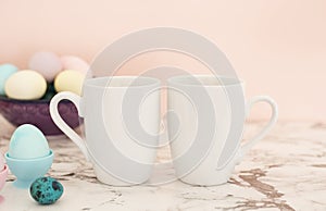Two White Mugs Mockup - Easter theme. Easter eggs. Colorful eggs in matte colors. Light marble background