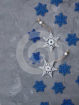 Two white ornaments on a Christmas tree in the form of snowflakes and many blue snowflakes lie on a gray concrete background.