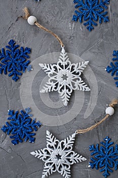 Two white ornaments on Christmas tree in the form of snowflakes and many blue snowflakes lie on a gray concrete background