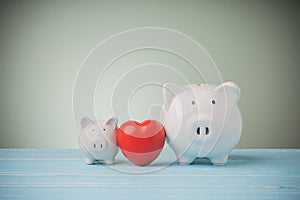 Two white piggys banks with red heart on blue wooden table green background with copy space. Concept love, money savings everyone