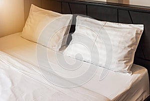 Two white pillows with white bedding sheet on empty bed in bedroom
