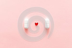 Two white pills on pink background with red heart shape, cardiac medications or femine cure photo