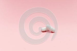 Two white pills on pink background with red heart shape, femine cure photo