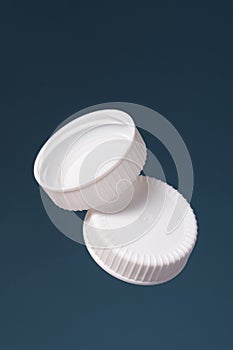 Two white plastic bottle caps on a blue background. Front and back of the cap.